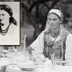 Chłopomania w weselu: młoda kobieta w tradycyjnym stroju, z naszyjnikami i chustą na głowie, siedzi przy stole nakrytym do obiadu.