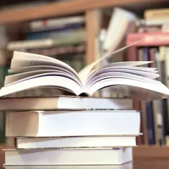 Otwarta książka na stosie innych, w tle regały pełne literatury, w tym klasyka jak "Zbrodnia i kara" gatunek.