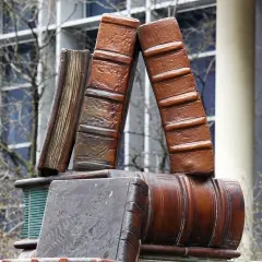 Pomnik w kształcie książek, symbol wiedzy trwalszy niż ze spiżu, stoi przed budynkiem z oknami.