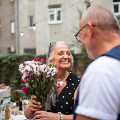 Uśmiechnięta kobieta z bukietem kwiatów, słuchająca mężczyzny. Idealny moment, by przypomnieć sobie o cytatach o docenianiu drugiej osoby.