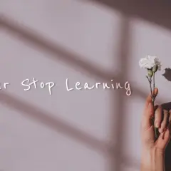 Dłoń trzyma biały kwiat. Napis "Never Stop Learning" przypomina o mądrych cytatach o szkole i ciągłym rozwoju.