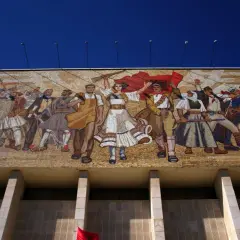 Mozaika w stylu socrealizmu przedstawia grupę ludzi w strojach ludowych, z bronią i flagami, symbolizujących walkę i jedność.