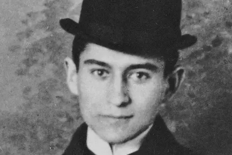 Młody mężczyzna w meloniku, przypominający bohatera powieści "Proces", patrzy zamyślony w obiektyw.