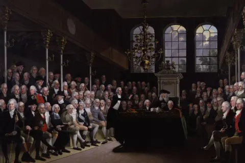 Wielu mężczyzn w perukach i strojach z epoki siedzi w sali, słuchając mówcy. Obraz oddaje ducha oświecenia w Polsce.