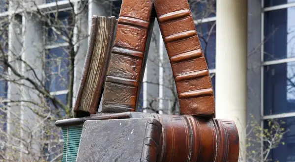 Pomnik w kształcie książek, symbol wiedzy trwalszy niż ze spiżu, stoi przed budynkiem z oknami.