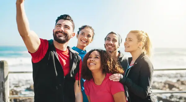 Grupa przyjaciół robi sobie selfie nad morzem. Ich uśmiechy to najlepsze cytaty o sobie, pełne radości i wspólnych chwil.