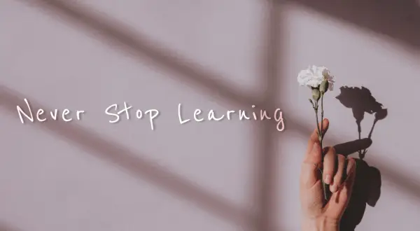Dłoń trzyma biały kwiat. Napis "Never Stop Learning" przypomina o mądrych cytatach o szkole i ciągłym rozwoju.
