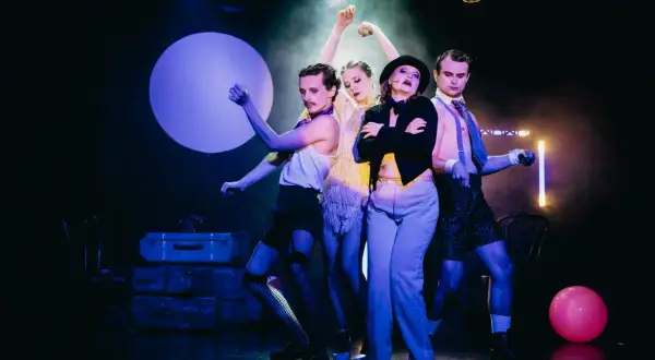 Czterech artystów na scenie, w teatralnych strojach, tworzy atmosferę o nierządne królestwo i zginienia bliskie.