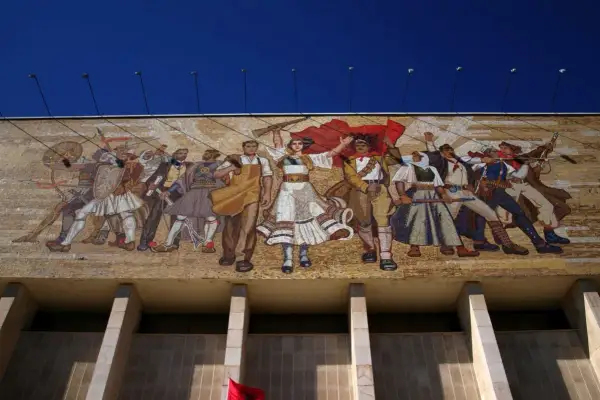 Mozaika w stylu socrealizmu przedstawia grupę ludzi w strojach ludowych, z bronią i flagami, symbolizujących walkę i jedność.